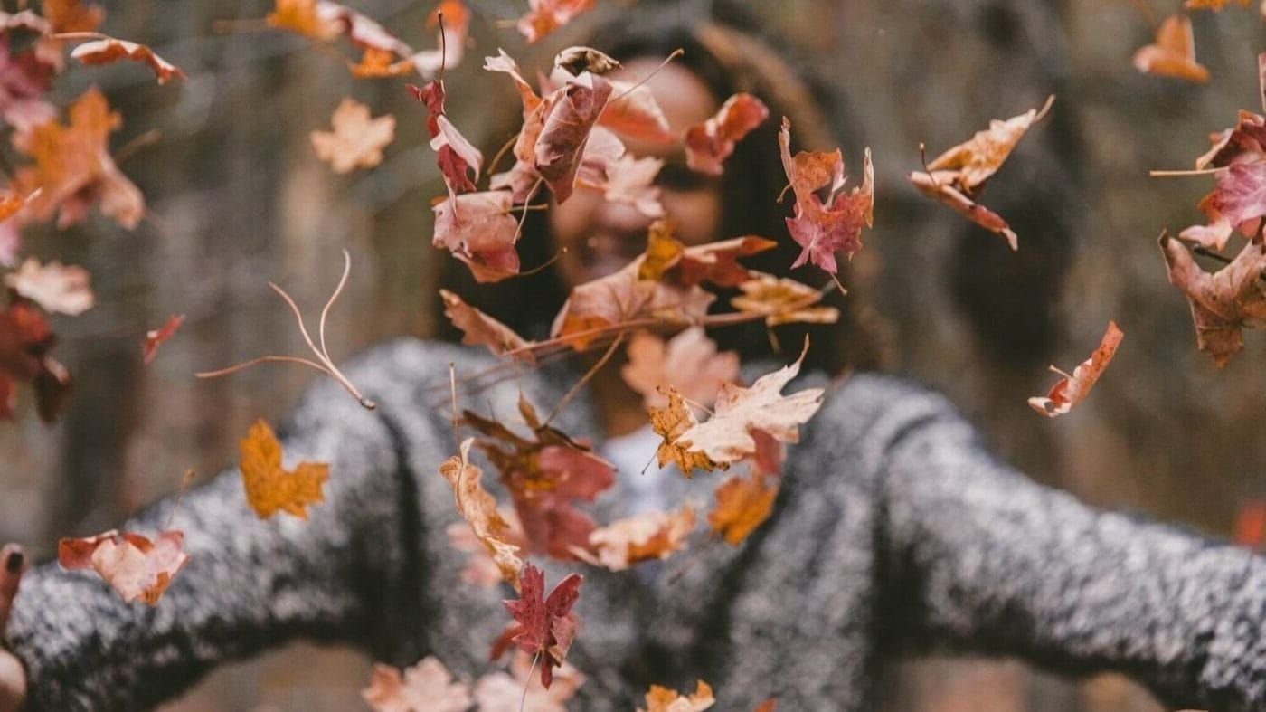 woman tossing brown and orange leaves into the air during autumn