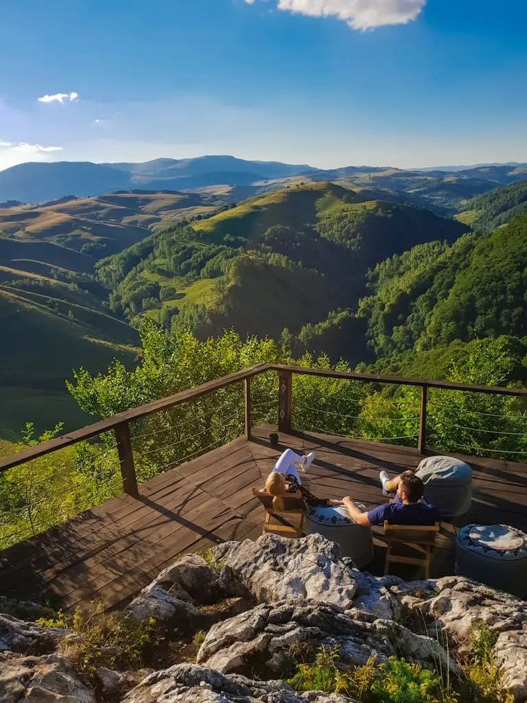 High Angle Photo Of A Man And Woman Sitting on Balcony Viewing Mountains Under Blue and White Sky