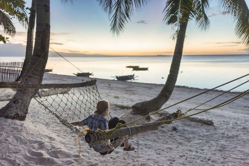 Margherita sitting in a hammock on the beach looking at the sunset with boats in the water