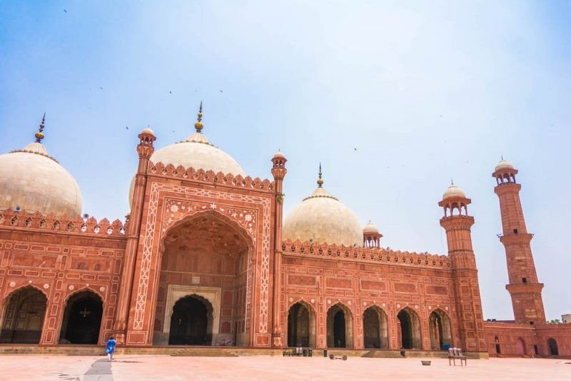 A pinkish red mosque in Pakistan with minarets and arches and domes