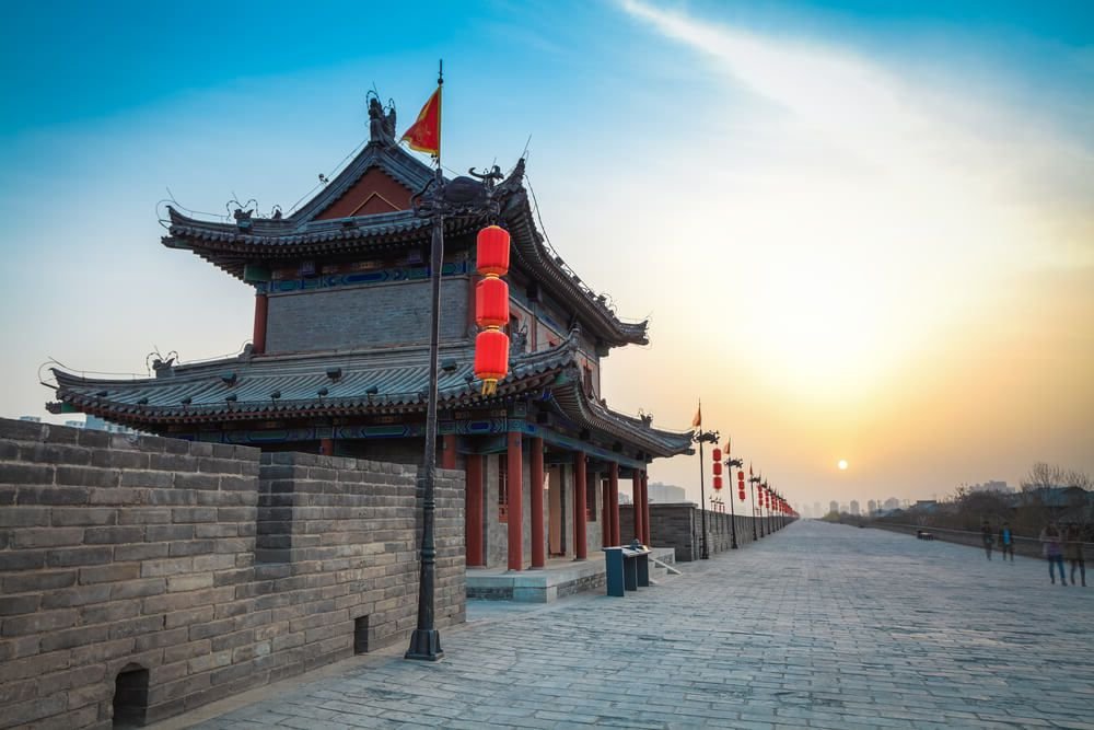view of the skyline in xian with old city walls and an ancient tower on the wall, red lanterns, around sunset