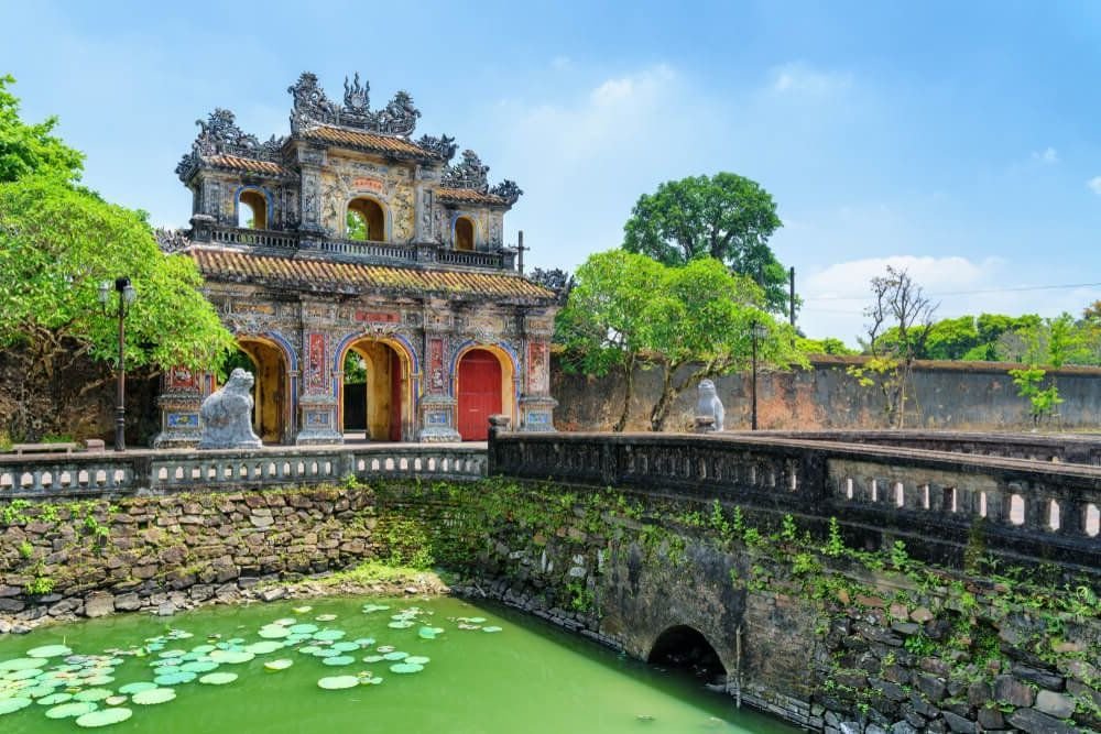 fancy gate to an imperial city in vietnam with a bridge with green water and lily pads in the water
