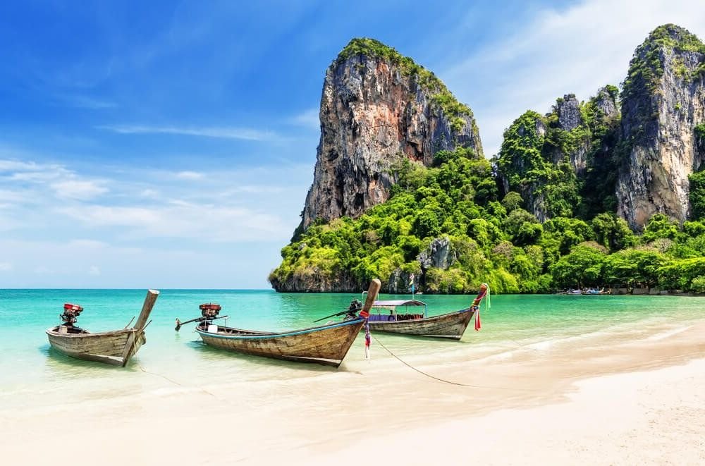 three famous thai longtail boats with the cliffside rock formations against the striking blue water