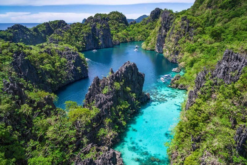 The El Nido part of Palawan, Philippines with an aerial view of beautiful turquoise lagoon and limestone cliffs covered in greenery.